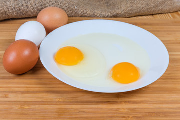 Whole eggs and broken eggs on dish on wooden surface