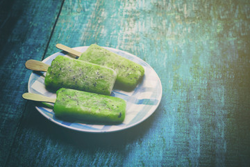 Fruit ice cream from kiwi, fruit ice on a stick,popsicle, lying on a plate on blue wooden vintage background