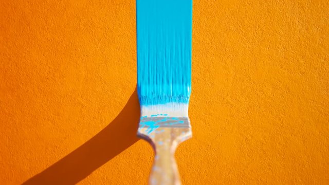 Wooden paintbrush leaving stripe of colorful cyan paint on an orange wall. 4KHD