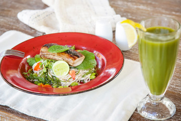 Grilled fish with green vegetable mix served with a glass of green detox smoothie, casual healthy dining concept