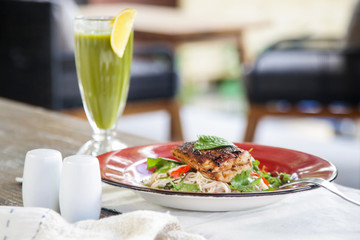 Grilled fish with green vegetable mix served with a glass of green detox smoothie, casual healthy dining concept
