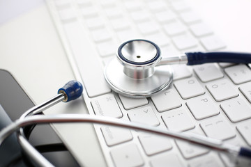 Medical stethoscope head lying on silver keyboard at doctor office worktable