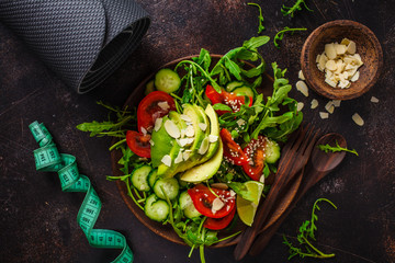 Green salad with avocado, tomatoes, cucumbers and nuts in wooden plate, centimeter on dark background. Fitness and diet food concept.