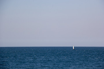 Fototapeta premium Small sailing yacht with big white sails in the open sea on the horizon