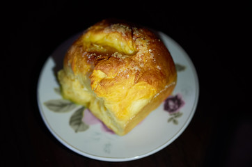 lush bun with sugar lies on a saucer on black background