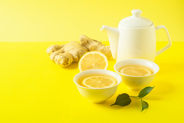 Ginger lemon tea or detox drink in a white cup and a teapot on a bright yellow background. Healthy eating concept.