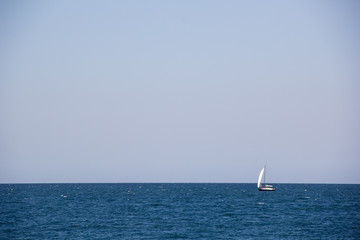 Fototapeta premium Small sailing yacht with big white sails in the open sea on the horizon