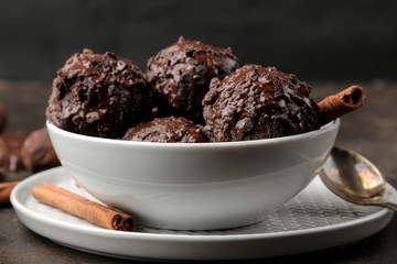 Chocolate ice cream with liquid chocolate with a cinnamon stick and coffee beans on a dark background.