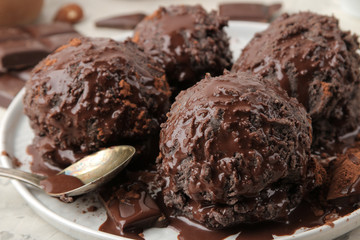 Chocolate ice cream with liquid chocolate and cinnamon sticks on a light concrete background.