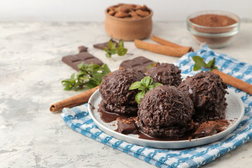 Chocolate ice cream with liquid chocolate and cinnamon sticks on a light concrete background.