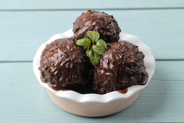 Chocolate ice cream with liquid chocolate and cinnamon sticks on a light concrete background.