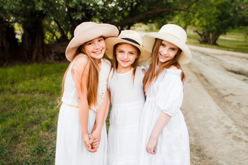 Three girls in white dresses walk in nature in the summer. Children's pastime during the summer holidays.