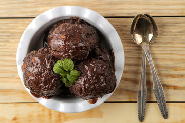 Chocolate ice cream with liquid chocolate and cinnamon sticks on a light concrete background.