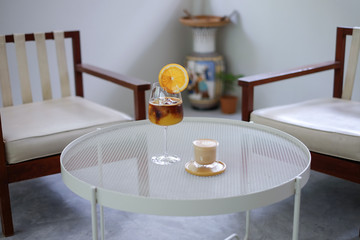 A wine glass of iced espresso shot with orange juice decorated with orange slide   and a glass of iced coffee latte on white table in living room, relaxing drink with selective focus.
