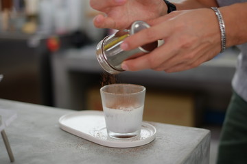 Pouring cocoa powder over a  glass of iced fresh milk. Selective focus.