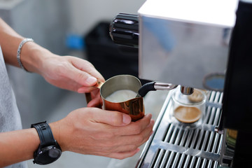Barista steaming milk in pitcher, reaches proper temperature degrees Fahrenheit for making coffee latte 