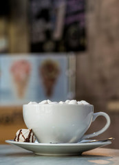 Mug of coffee with marshmallows on porcelain plate on blurred colorful interior bokeh background.