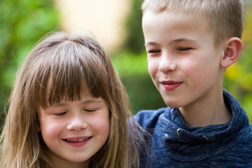 Two cute fair-haired children siblings, young boy brother and sister girl outdoors on bright sunny green bokeh background. Family relation, friendship and love concept.