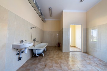 Interior of spacious light hospital or kindergarten bathroom with white bathtub, sink, air ventilation duct and tiled floor and walls.