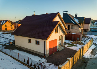 Aerial view of new residential house cottage and attached garage with shingle roof on fenced yard on sunny winter day in modern suburban area. Perfect investment in dream house.