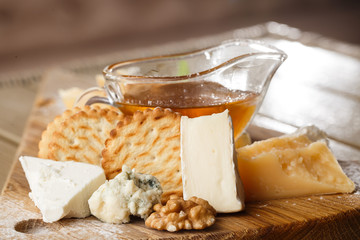 Tasting cheese dish on a wooden plate. Food for wine and romantic, cheese delicatessen on a wooden rustic table. Top view with copy space.