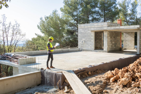 Apprenti artisan, m&eacute;tier du b&acirc;timent v&eacute;rifiant un plan sur un chantier de maison en construction