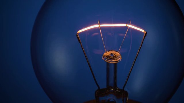 flickering tungsten filament of classic incandescent lamp on blue background close up. bad electrical contact immitation