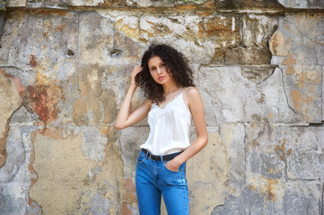 Young woman in jeans and white blouse at the old textured wall