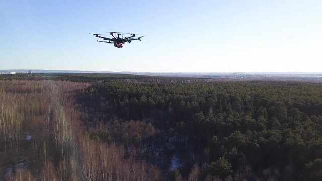 Aerial for the drone camera flying in the sky above deciduous and coniferous forest on blue sky background. Clip. Spinning quadcopter blades, slow motion.