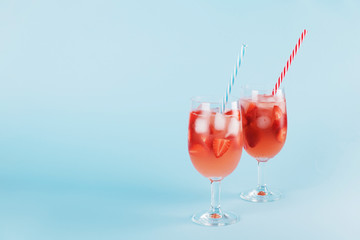 Fresh strawberry summer cocktail and ice cubes. Two glasses with strawberry, ice and wine - strawberry sangria on a pastel blue backgound, minimalism