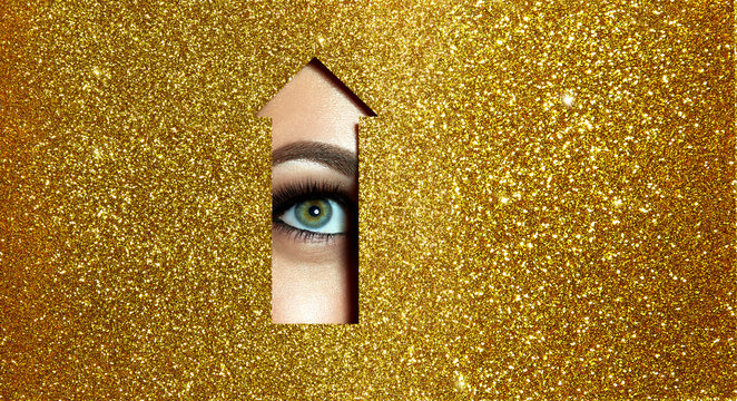 The girl says &ldquo;look up.&rdquo; A girl with beautiful full lips painted red lipstick with a metallic effect and green eyes looks up through a cut in golden shiny paper in the form of an arrow. Arrow pointer.