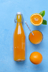 Orange juice in glass bottle with fruits on bright blue background