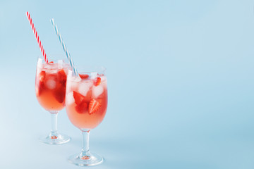 Fresh strawberry summer cocktail and ice cubes. Two glasses with strawberry, ice and wine - strawberry sangria on a pastel blue backgound, minimalism