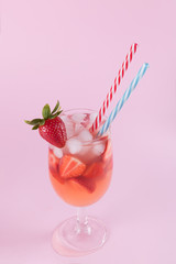 Fresh strawberry summer cocktail and ice cubes. Glass with strawberry, ice and wine - strawberry sangria on a pastel pink backgound, minimalism