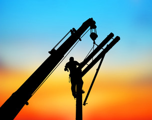 Silhouette Electrical engineers working on electricity pylon high tension power line repairs and maintenance  on blurry sunset background