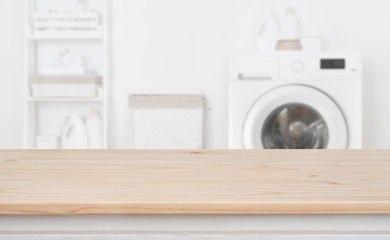 Wooden table in front of defocused washing machine and laundry - obrazy, fototapety, plakaty