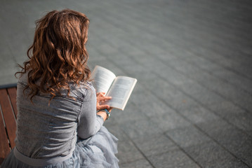 Young woman reading a book on a bench, back view