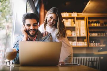 Couple have fun while looking on laptop at cafe