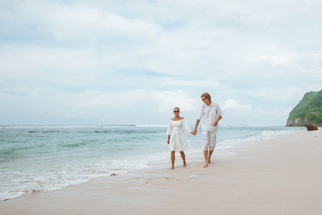 Girl and man in white clothes walking on white beach in Bali and holding hands