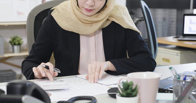 unrecognized muslim business woman leader using calculator do math finance on desk in office working. tax accounting statistics and analytical research concept. islam lady with headscarf counting