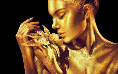 Fashion model woman with bright golden sparkles on skin posing, fantasy flower. Portrait of beautiful girl with glowing makeup. Art design gold sequins make up. Glitter glowing golden skin © Subbotina Anna