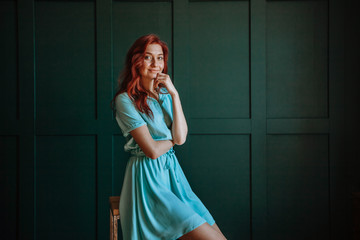 Portrait of a beautiful redhaired girl in a light blue dress on a dark background