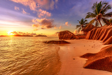 Seychellen, La Digue, Anse Source d& 39 Argent bij zonsondergang. Landschap met lucht en kleurrijke wolken op rotssteen van graniet met palmbomen. Zon bij schemering op de kalme zee aan de horizon.