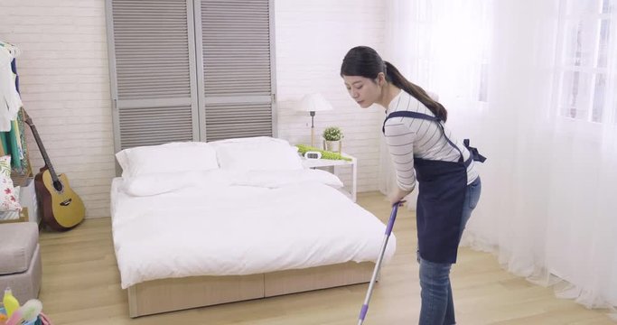 slow motion young asian elegant woman housewife cleaning wooden floor with mop in cozy bedroom. proud professional housemaid doing room service tidy up apartment looking at camera smiling attractive