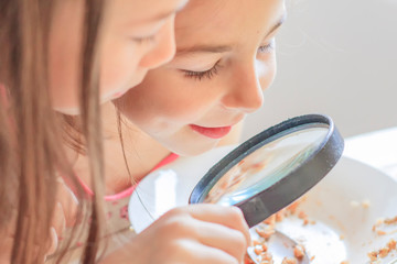 Children are considering a magnifying glass leftover food on a plate
