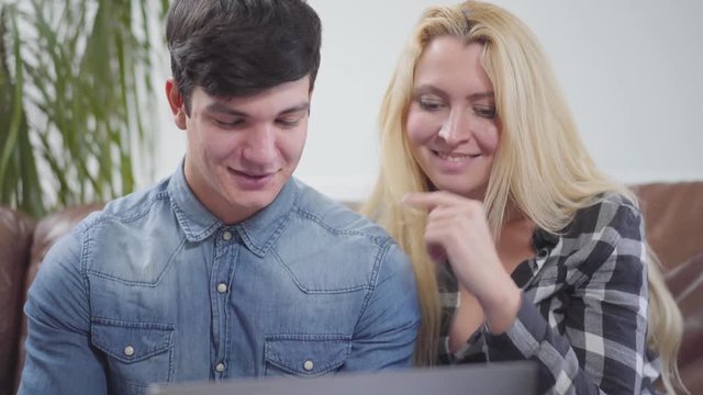 Adorable couple sitting in front of a laptop at home. Portrait of a brunette man and blond woman discussing the project on the notebook. Working with gadgets