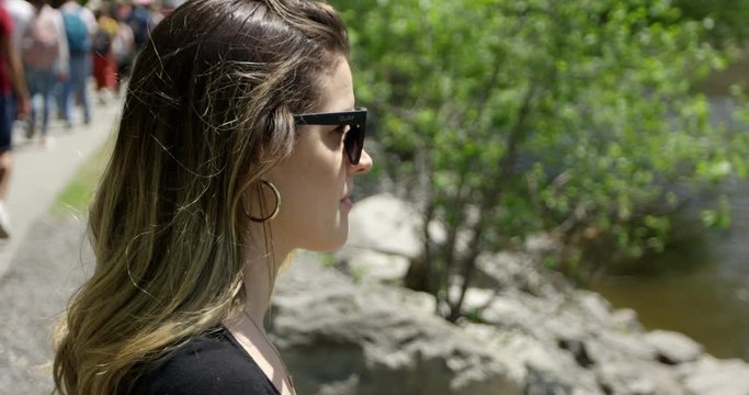 Stylish young woman looks out into water on busy walking path - side profile