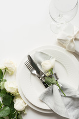 Romantic and wedding table setting with white rose, gift, dishware, silverware on white table. Top view.