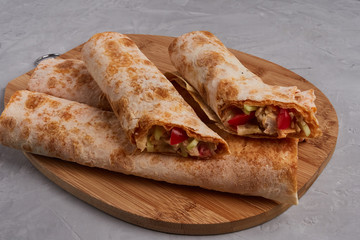 Shawarma, fresh roll of pita, chicken, vegetables. Traditional Middle Eastern snack on a wooden board