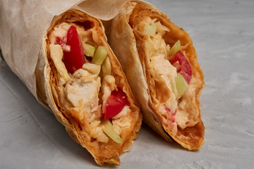 Shawarma, fresh roll of pita, chicken, vegetables. Traditional Middle Eastern snack on gray background close up.